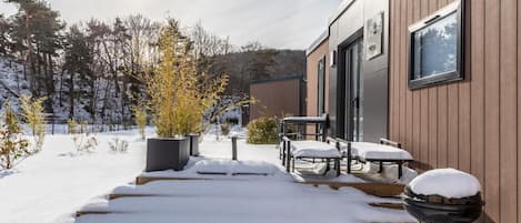 Un edificio moderno con fachada de madera, un área de estar al aire libre techada y un paisaje nevado.