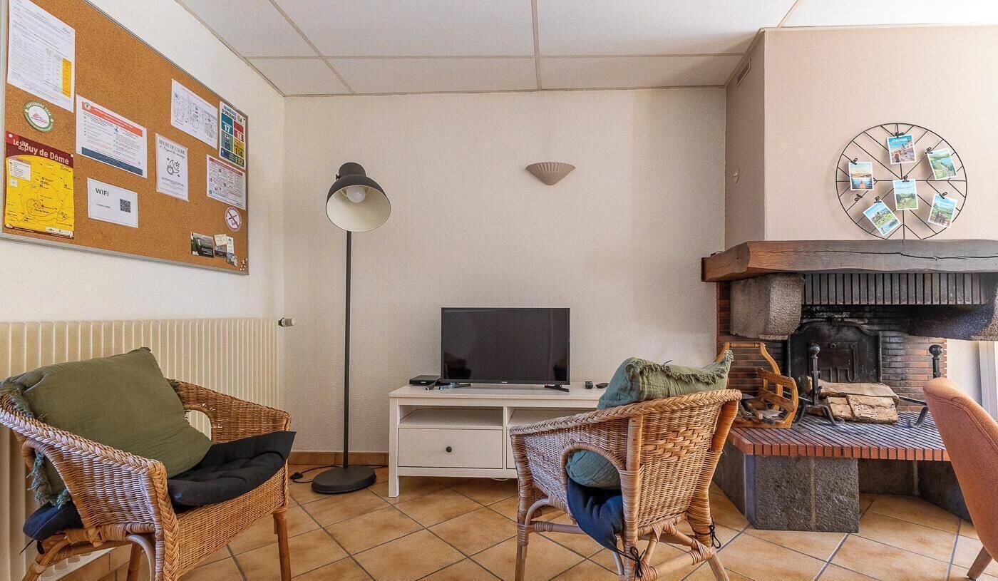 Una sala de estar acogedora con muebles de mimbre, un televisor de pantalla plana, una chimenea y un tablón de anuncios con varios avisos.
