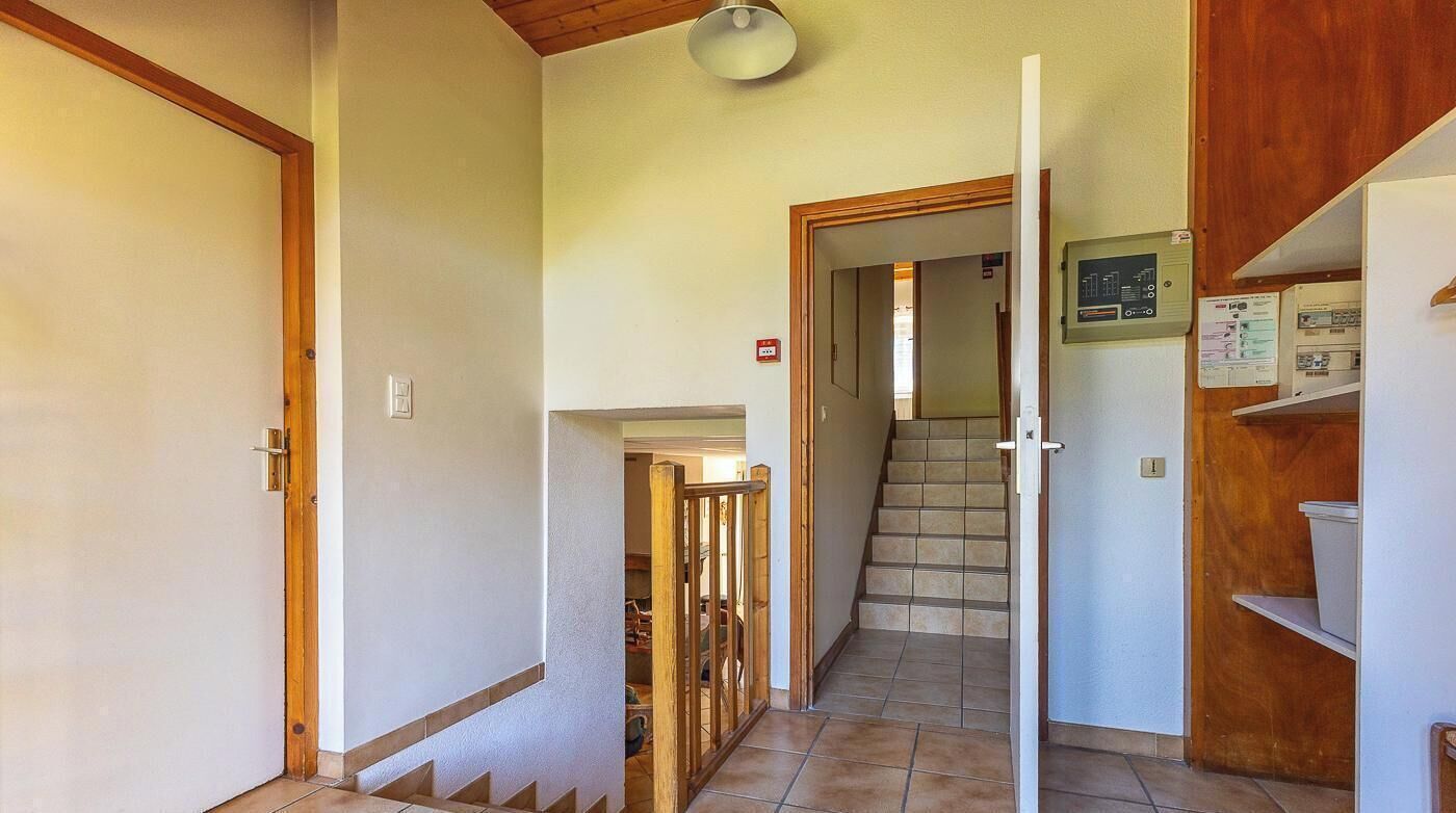 A hallway with a staircase, wooden doors, and a utility panel on the wall.