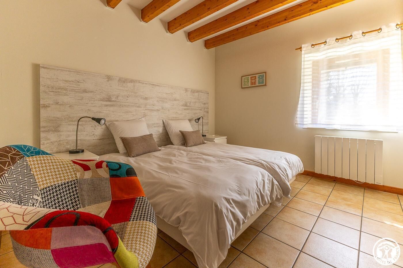 Un dormitorio con cama, mesita de noche, lámpara, radiador y ventana con cortinas.