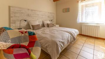 Un dormitorio con cama, mesita de noche, lámpara, radiador y ventana con cortinas.