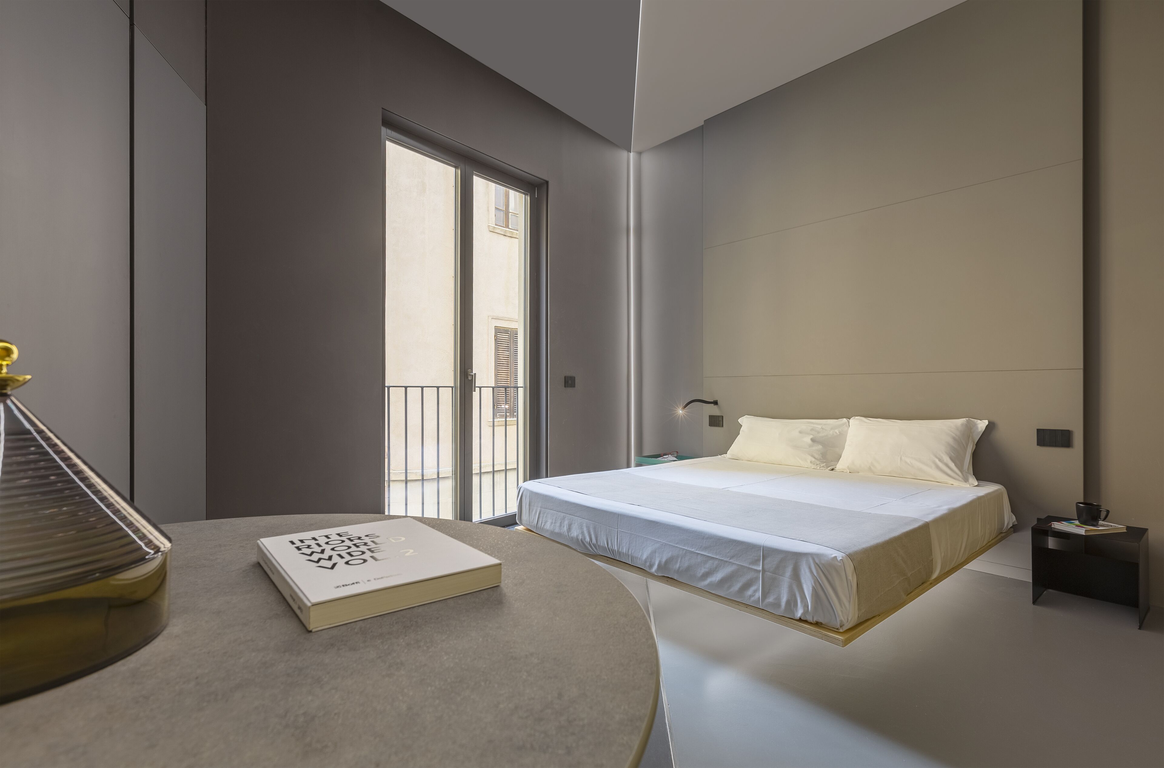 A modern bedroom with a bed, a bedside table, a book, and a window.