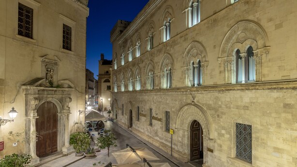 A historic building with arched windows and a courtyard with potted plants and umbrellas. - Fiveplace Design Suite & Apartments (Trapani)
