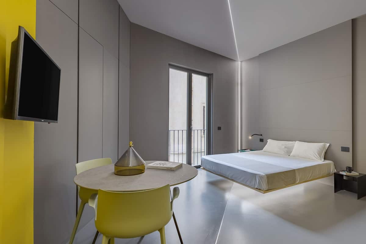 A modern hotel room with a bed, bedside table, and a TV mounted on the wall.