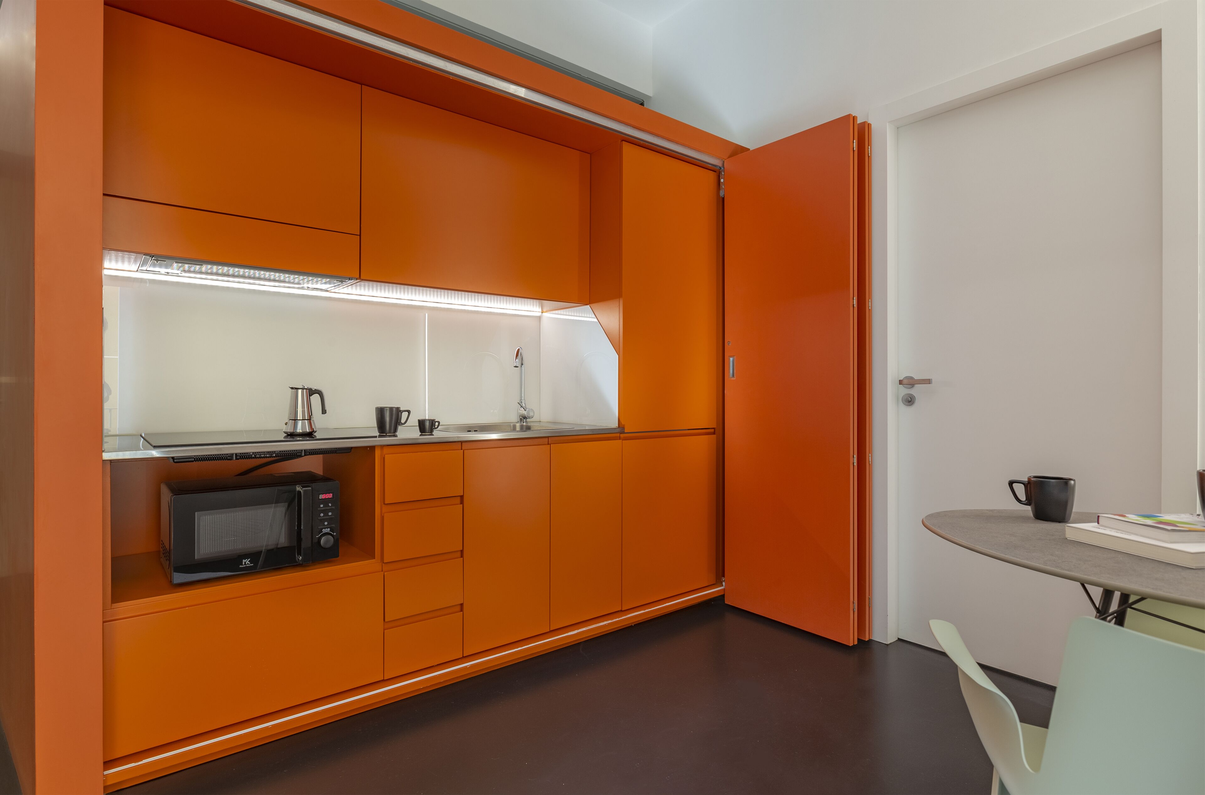 A compact kitchen with orange cabinetry, a microwave, and a small countertop.