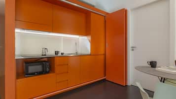 Uma cozinha compacta com armários laranja, micro-ondas e bancada pequena.