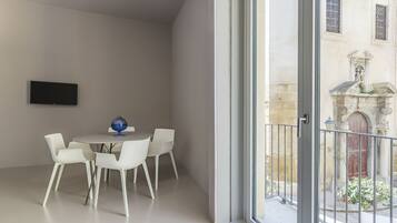 Una habitación moderna con una mesa de comedor redonda, sillas blancas, un televisor de pantalla plana y un gran ventanal con vistas a un patio que tiene una estatua y plantas.