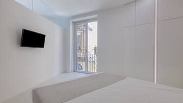 A modern bedroom with a bed, a flat-screen TV mounted on the wall, and a large window providing a view of the outside.