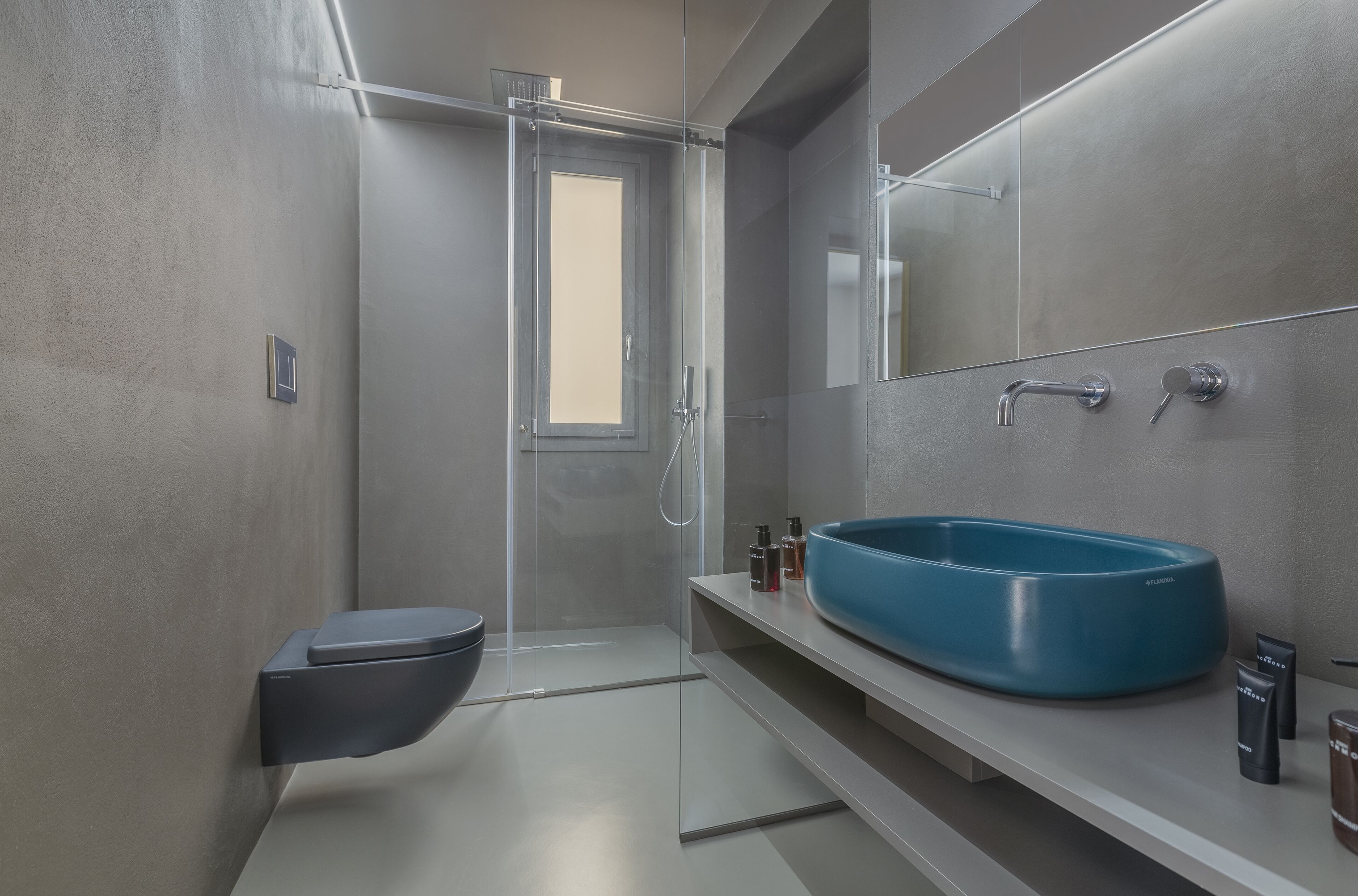 Un baño moderno con cabina de ducha de vidrio, un lavamanos tipo cuenco azul y un inodoro.