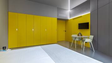 A modern room with yellow and grey walls, a white table with chairs, and a flat-screen TV mounted on the wall.
