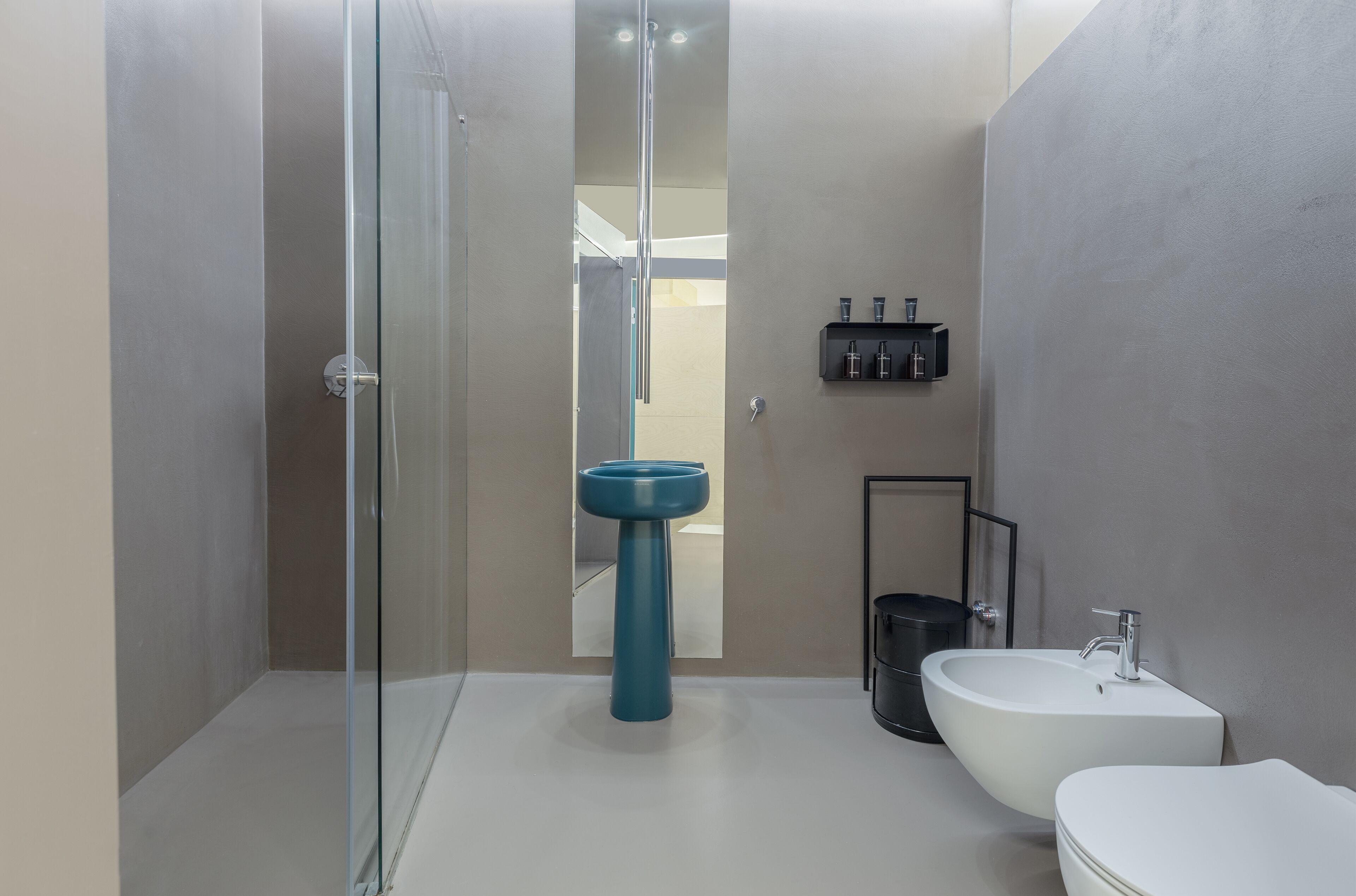Casa de banho moderna com chuveiro envidraçado, lavatório branco e lavatório pedestal azul.