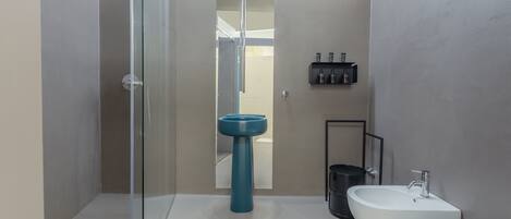 Casa de banho moderna com chuveiro envidraçado, lavatório branco e lavatório pedestal azul.