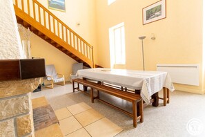 A room with a wooden staircase, a table with a white tablecloth, a bench, and a radiator.