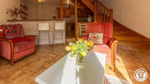 A cozy living room with two armchairs, a coffee table with a vase of flowers, and a kitchen area with a wooden staircase. - Les Hirondelles - Murol (MUROL)