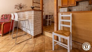 A kitchen with a stone wall, wooden cabinets, and a white chair. - Les Hirondelles - Murol (MUROL)