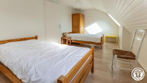 A bedroom with two wooden beds, a wooden wardrobe, a wooden chair, and a small yellow table. - Les Hirondelles - Murol (MUROL)