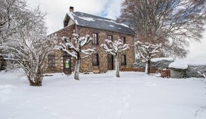 Un bùtiment en pierre, avec un toit enneigé et des arbres devant.