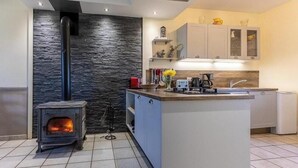 A modern kitchen with a central island, a built-in stove, grey cabinets, and a stone accent wall.