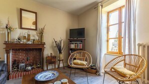 A cozy living room with a fireplace, wicker chairs, a television, and a bookshelf.