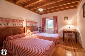 Two single beds with striped bedding and a wooden headboard, situated near a window with curtains.
