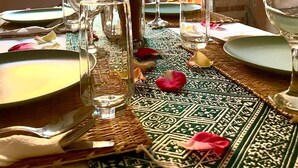 A dining table set with clear glasses, plates, and a pitcher, with a patterned table runner and rose petals. - Riad Rihana Tamlalte (Ait Sedrate Jbel El Soufla)