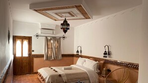 A bedroom with a bed, a chair, a small table, a window with curtains, and a ceiling fan. - Riad Rihana Tamlalte (Ait Sedrate Jbel El Soufla)