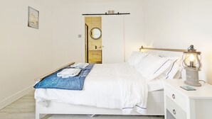 Un dormitorio con cama, mesita de noche, lámpara y una puerta que da a un baño.