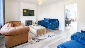 Una sala de estar moderna con un sofá marrón, un sofá azul, una mesa de centro de madera y un televisor montado en la pared.
