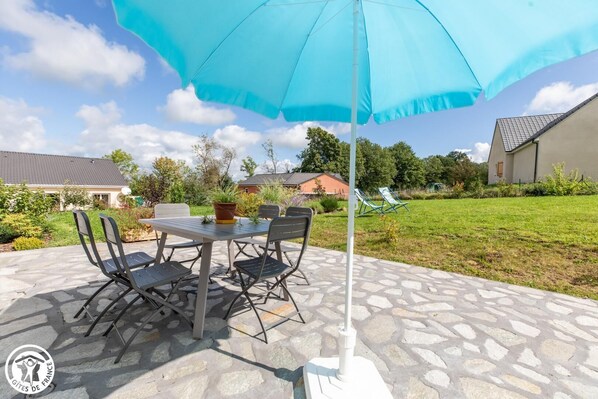 An outdoor patio with a table and chairs, a blue umbrella, and a stone floor.