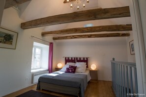 Cozy bedroom with a sloped ceiling and exposed beams, featuring a single bed and bedside tables with lamps.