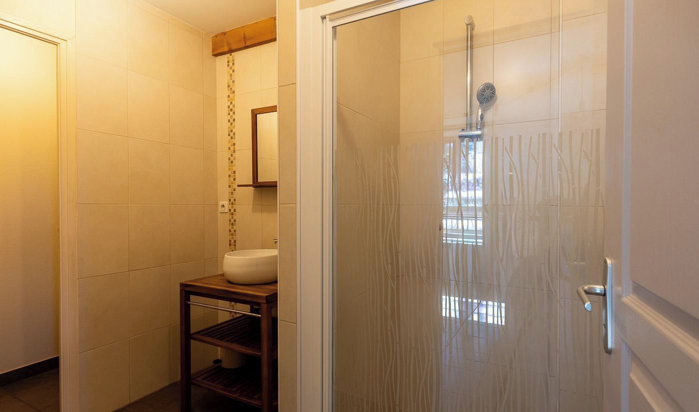 A bathroom with a glass shower enclosure, a white sink, and a wooden shelf.