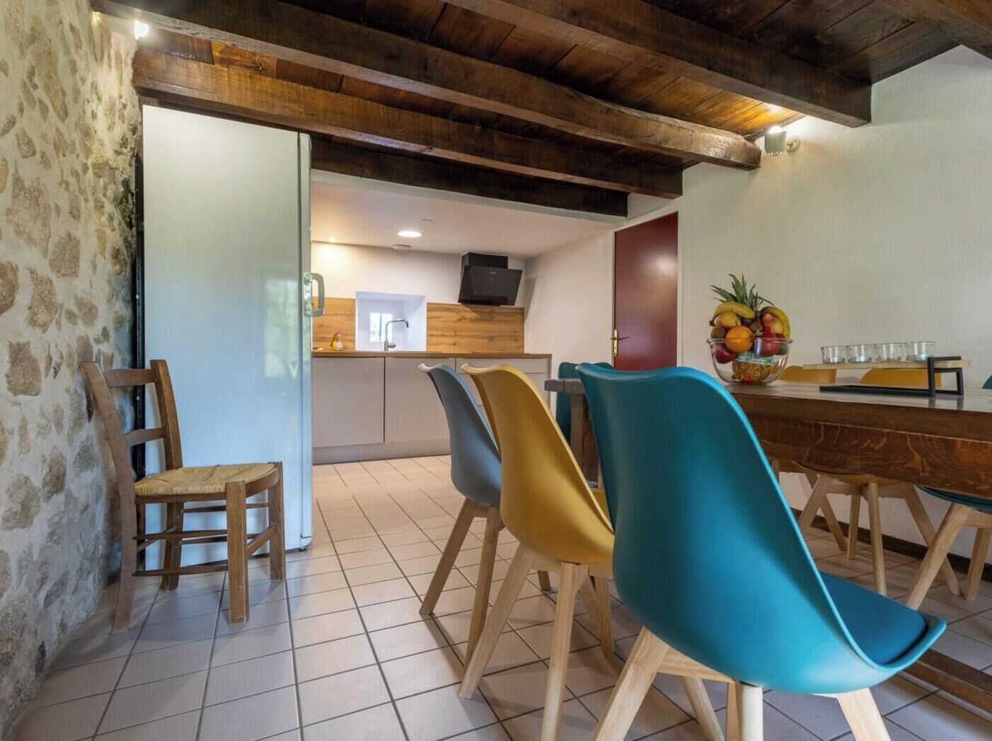 Un comedor con una mesa de madera, sillas coloridas y un frutero sobre la mesa.