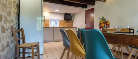 Un comedor con una mesa de madera, sillas coloridas y un frutero sobre la mesa.