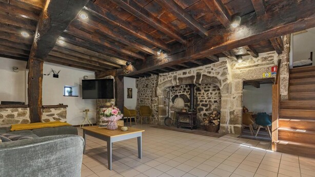 Un intérieur rustique avec des poutres apparentes, une cheminée en pierre, un téléviseur à écran plat et un canapé.