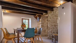 Un coin repas avec un mur en pierre, des poutres en bois au plafond, un réfrigérateur blanc et une table avec des chaises.