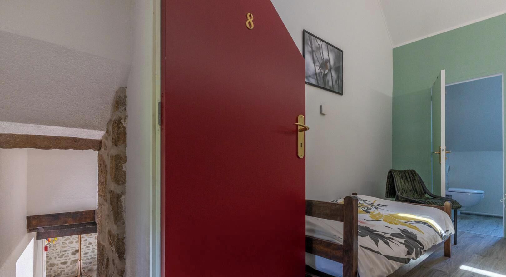 A room with a red door, a bed with a floral bedspread, a chair, and a green wall.