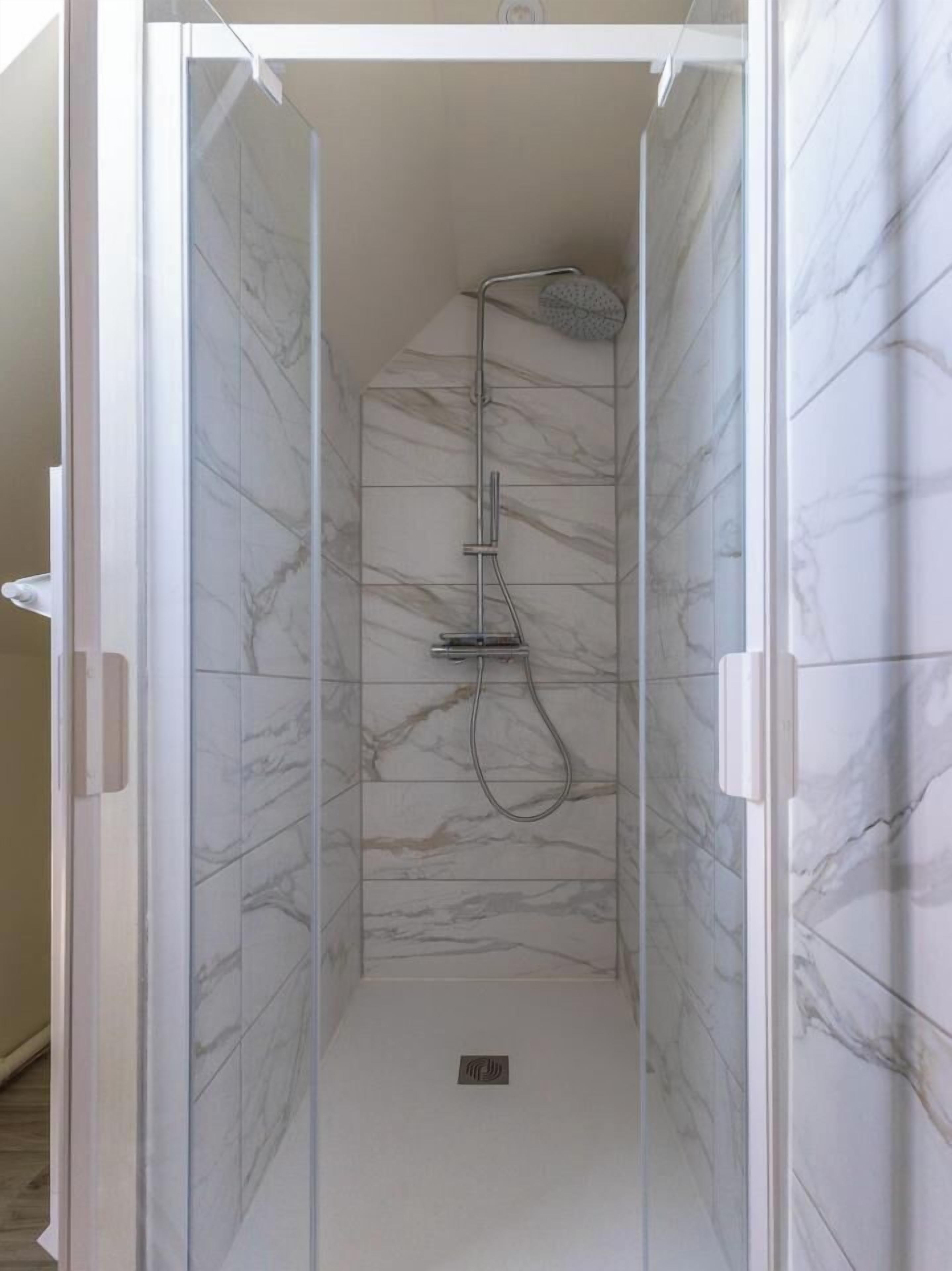 A glass-enclosed shower with marble tiles and a handheld showerhead.