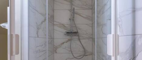 A glass-enclosed shower with marble tiles and a handheld showerhead.