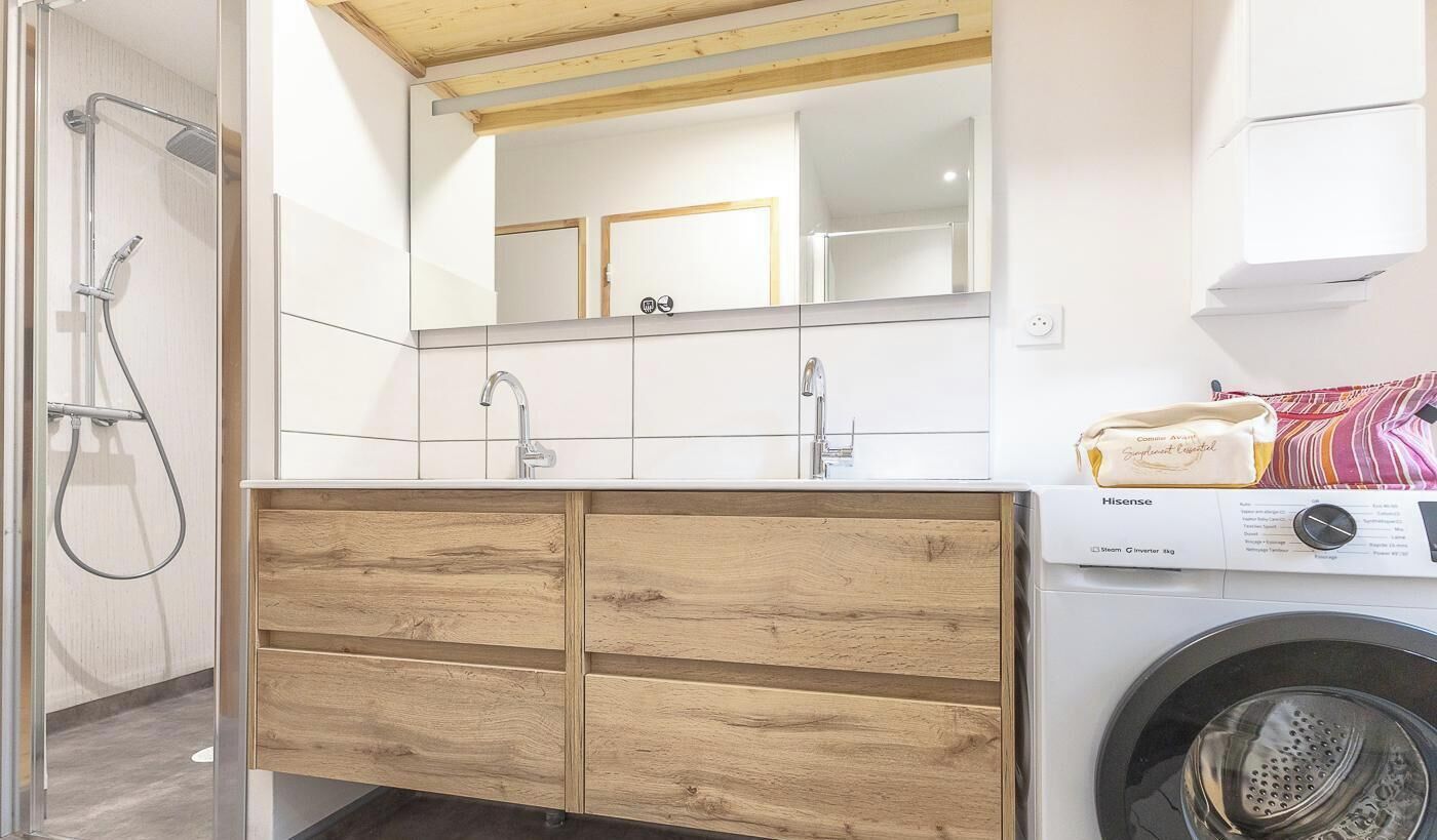 A modern bathroom with a wooden vanity, a mirror, a sink, and a washing machine.