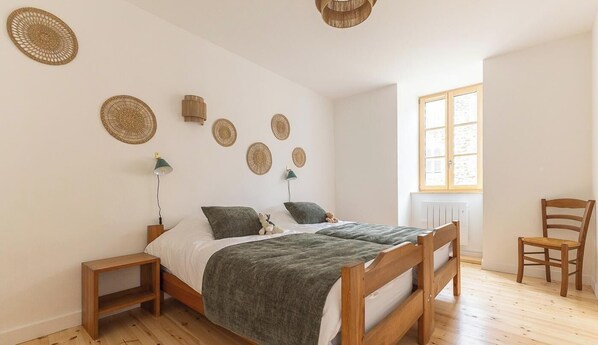 A bedroom with two beds, a wooden chair, a window, and wall decorations.
