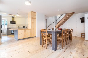 A modern kitchen with wooden cabinets, a dining area with a table and chairs, and a staircase.