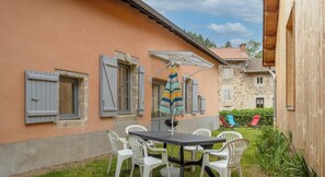 A patio with a table and chairs, a striped umbrella, and a stone building in the background.
