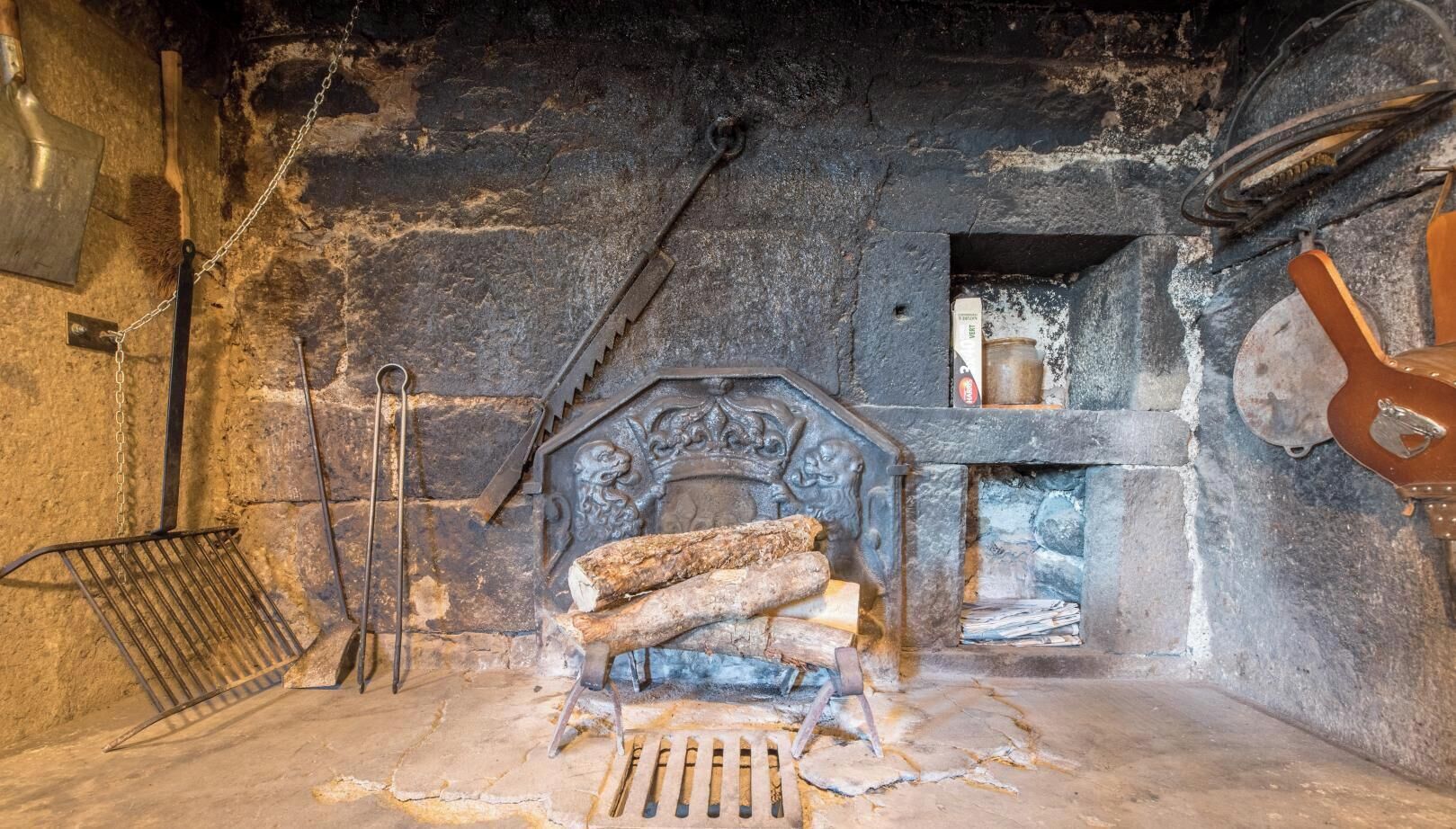 Ein Kamin aus Stein mit Holzscheiten, einem Metallgitter und einem Schornstein.