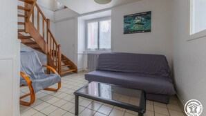 Um quarto com escada de madeira, um sofá cinzento, uma mesa de centro de vidro e um pôster na parede.