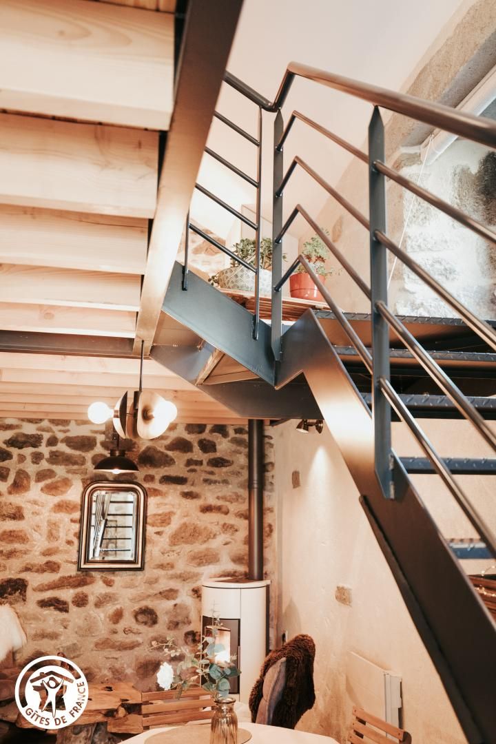 A staircase with a metal railing leading to a higher floor, a stone wall, and a wooden ceiling.