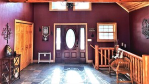 Une pièce avec un plafond en bois, un mur d’un violet foncé, une porte en bois dotée de panneaux de verre, un banc et une petite table.