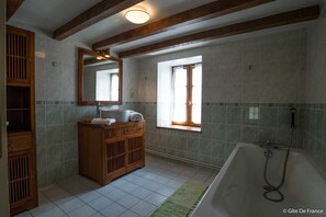 Bathroom features a large bathtub, vanity with mirror, and a window.