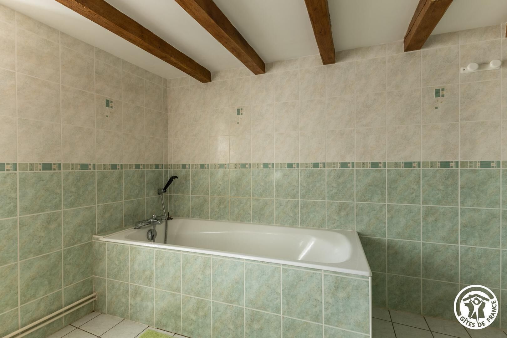 A bathroom with a bathtub, green tiles, wooden beams, and a visible electrical outlet.