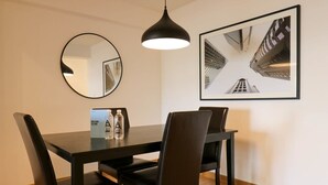 A dining area with a black table, four chairs, a round mirror, and a framed photograph on the wall.