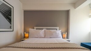 A neatly made bed with a headboard, two bedside lamps, and a framed picture on the wall.